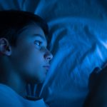 Boy using a smartphone at night in bed.