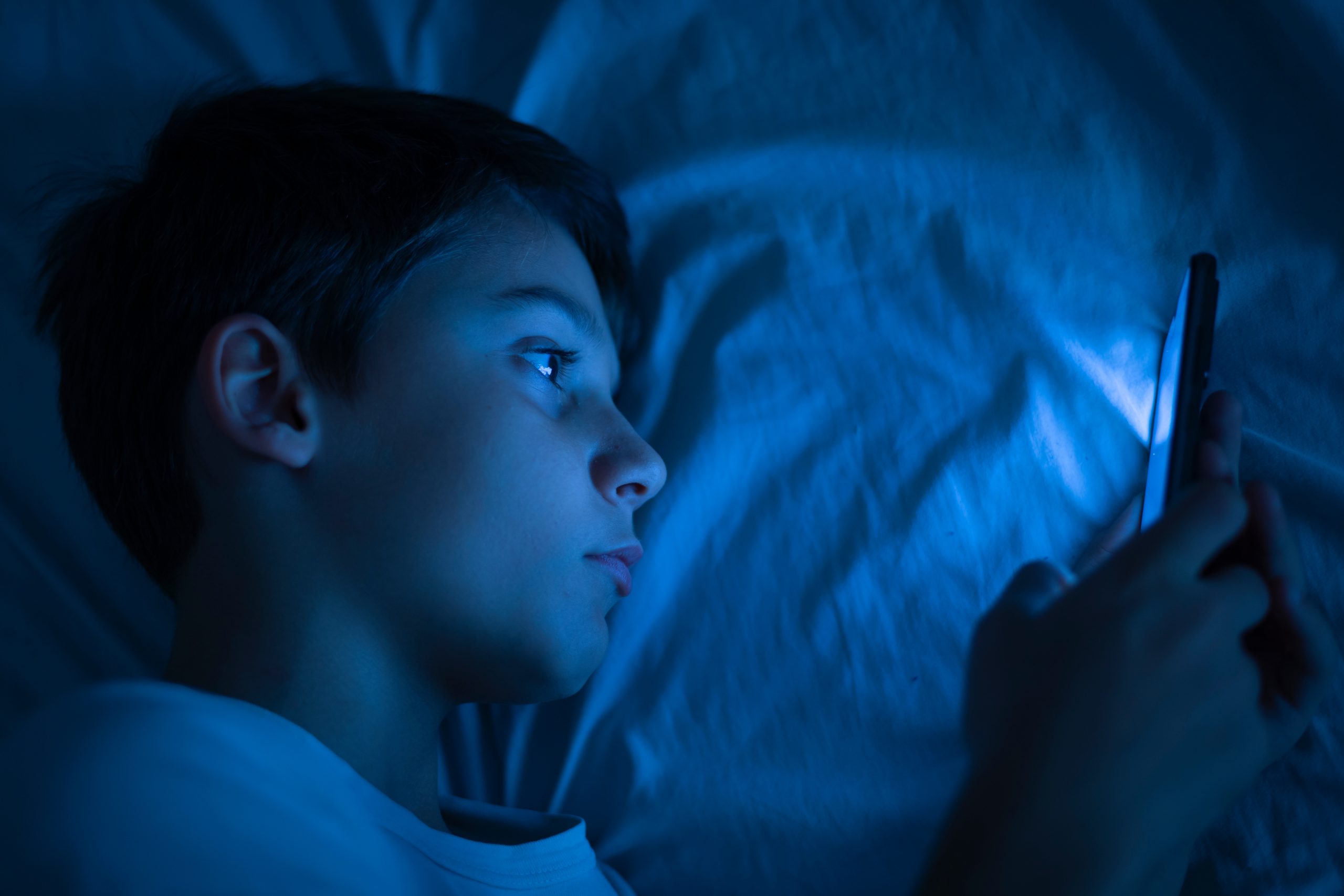 Boy using a smartphone at night in bed.